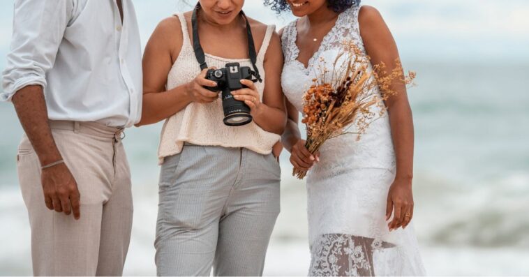 Photographer shows wedding photos to the bride and groom, on the beach.