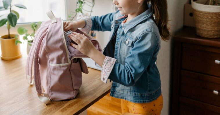 Smiling girl opening backpack on table at home.