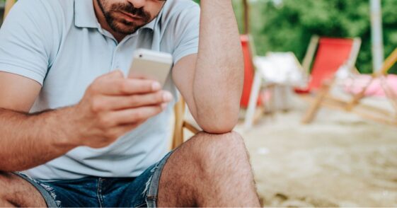 Annoyed man on the beach looking at a mobile screen.