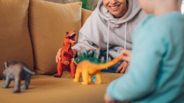 Mother and toddler son playing with dinosaurs toys at home on the couch.