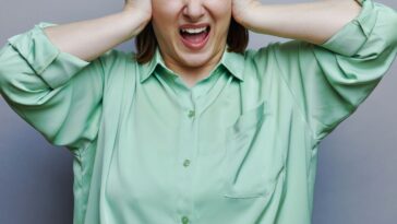 Woman screaming with eyes closed on grey studio background.