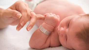 newborn infant holding an adult's finger