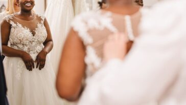 Shop assistant helping bride get into wedding dress.