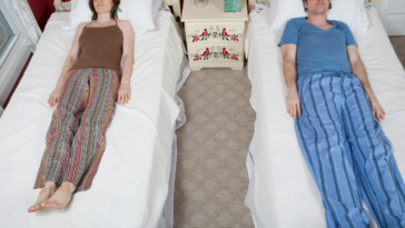 A man and a woman sleeping in twin beds.