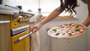 Young woman holding homemade pizza with mozzarella, chili peppers and basil.
