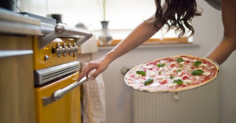 Young woman holding homemade pizza with mozzarella, chili peppers and basil.