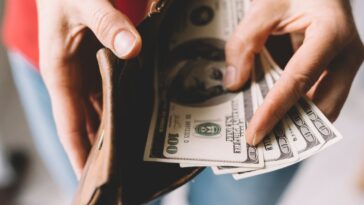 A pair of hands shows off several hundred dollar bills in a wallet.