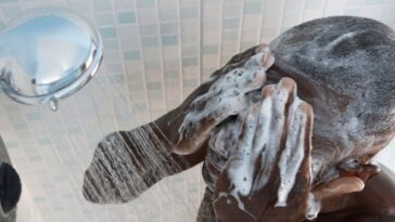 A man in the shower, washing his face.