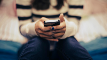 A teenage girl sitting on her bed, looking at her phone.