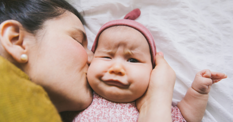 A woman kissing a baby with an awkward expression on her face.