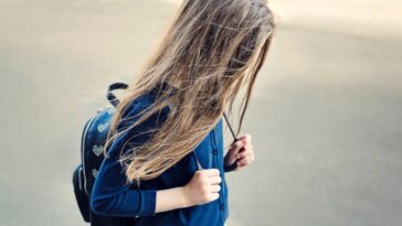 A sad teen girl walks with her backpack. Her long hair covers her face.