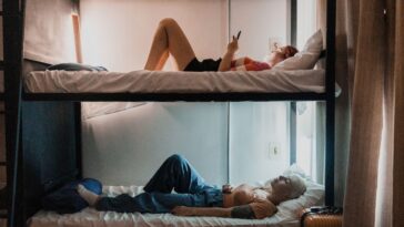 Roommates resting in bunk beds/using mobile phone in a hostel.