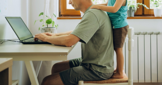 man working on laptop with child standing behind him