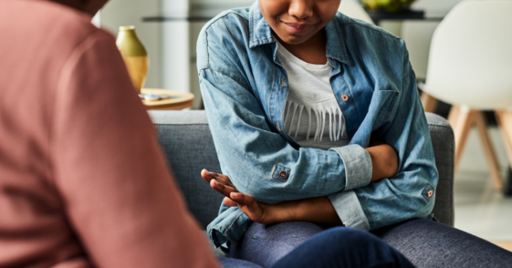 upset preteen girl seated on couch speaking to adult