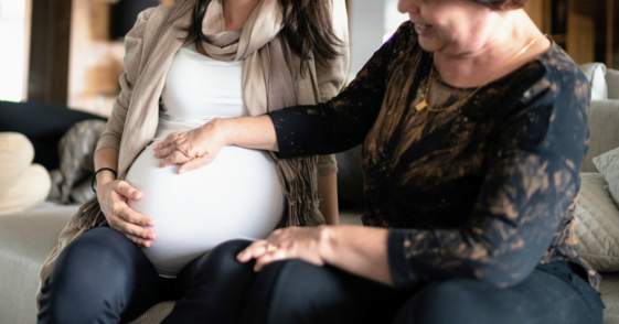 older woman with her hand on pregnant person's belly