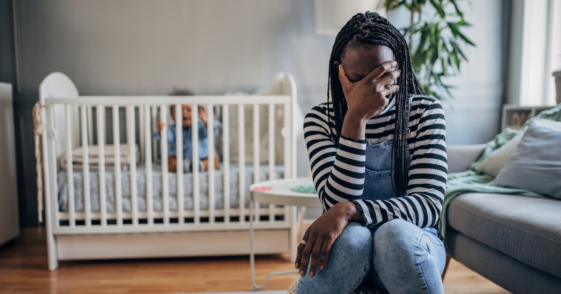 mother with face in hand in front of baby in crib