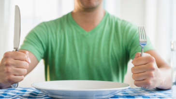 Man with empty dinner plate holding fork and knife