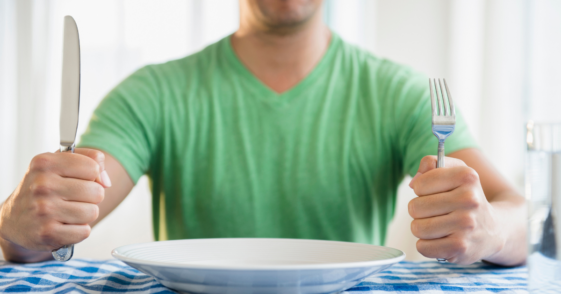 Man with empty dinner plate holding fork and knife