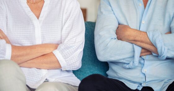 Mature couple fighting at home sitting on the sofa. They both have their arms crossed.