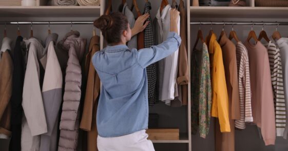 Young woman choosing clothes in wardrobe closet, back view.