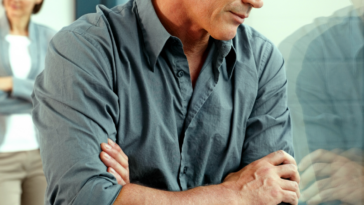 A man with his arms crossed leaning against a glass door, and a woman with her arms crossed standing behind him.