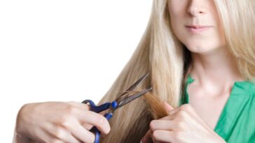 Blonde girl cuts off the tips of her hair.