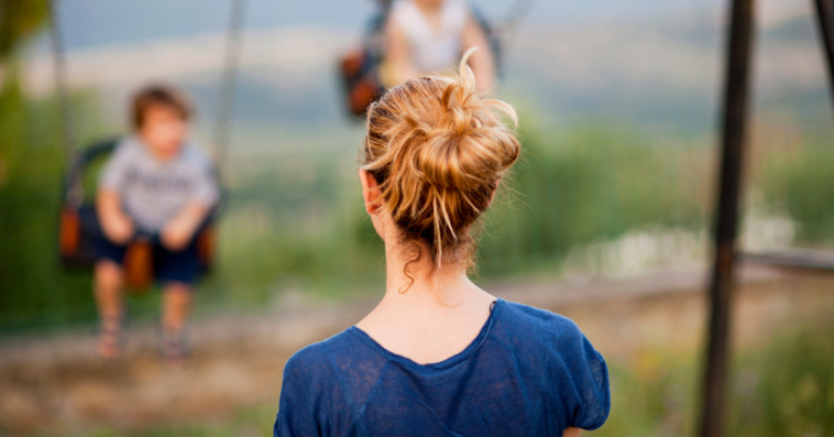 A woman looking at two children on swings.