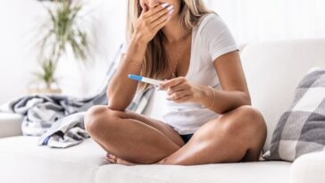 Woman sitting on a bed finding out she is pregnant from a test starts to cry from happiness.