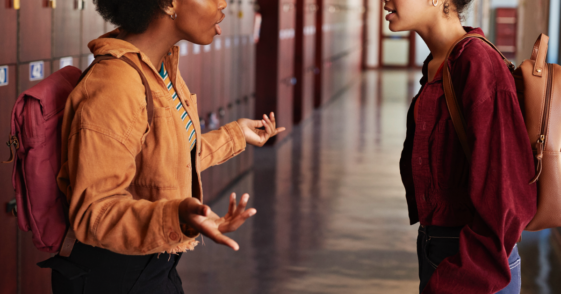 Two teenage girls in a school hallway having an argument.