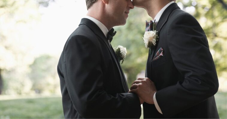 Newlywed grooms kissing outside.