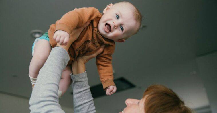 Grandmother lifting up baby at home.