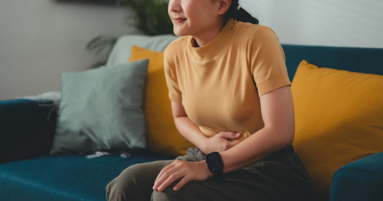 A woman sitting on a sofa, holding her stomach.