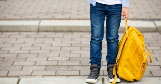 A child holding a yellow backpack at their feet.