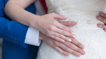 A groom standing behind a bride holding her stomach.