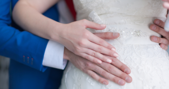 A groom standing behind a bride holding her stomach.