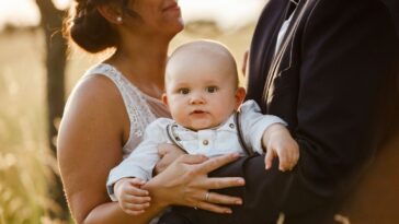 Midsection of parents carrying a baby boy and standing during a wedding at sunset.