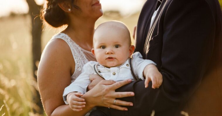 Midsection of parents carrying a baby boy and standing during a wedding at sunset.