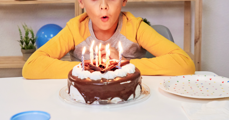 A little boy blowing out birthday candles on a chocolate cake.