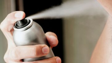 Mid section view of a young man spraying deodorant.