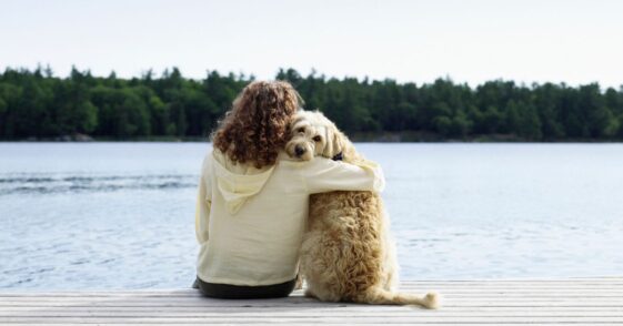 Woman hugging her dog while they on a jetty, rear view.