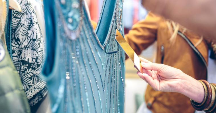 A woman looking at a price tag of a dress on a rack.