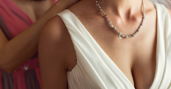 A woman putting a diamond necklace on a bride.