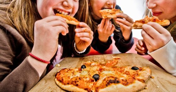 Three teenage girls eating pizza.