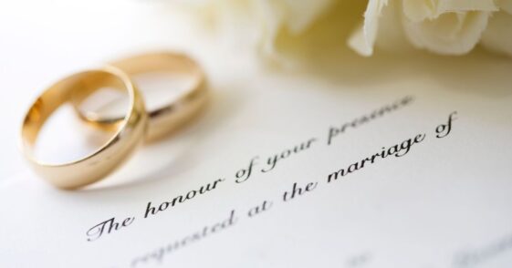 Wedding invitation with rings and a white rose bridal bouquet.