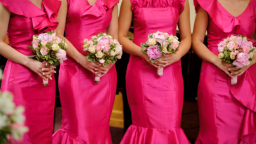 A line of bridesmaids standing in a row, wearing pink dresses and holding bouquets.