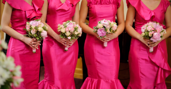 A line of bridesmaids standing in a row, wearing pink dresses and holding bouquets.