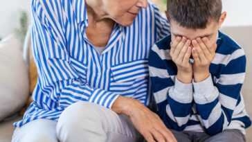 Loving, understanding grandma embracing little crying boy while sitting on couch.