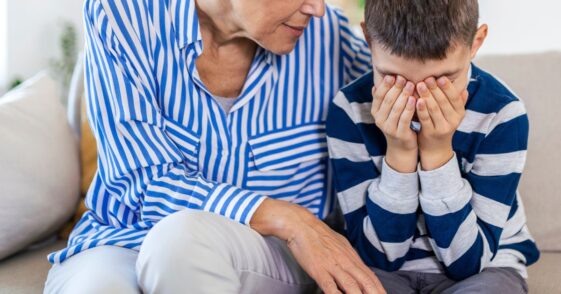 Loving, understanding grandma embracing little crying boy while sitting on couch.