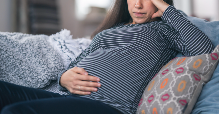 A pregnant woman lying on the sofa with one hand on her stomach, and one hand holding her head.