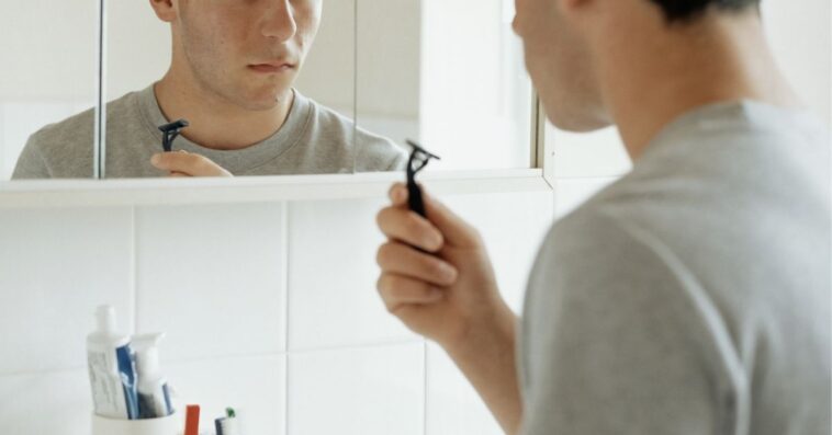 Teenager facing mirror while holding razor blade